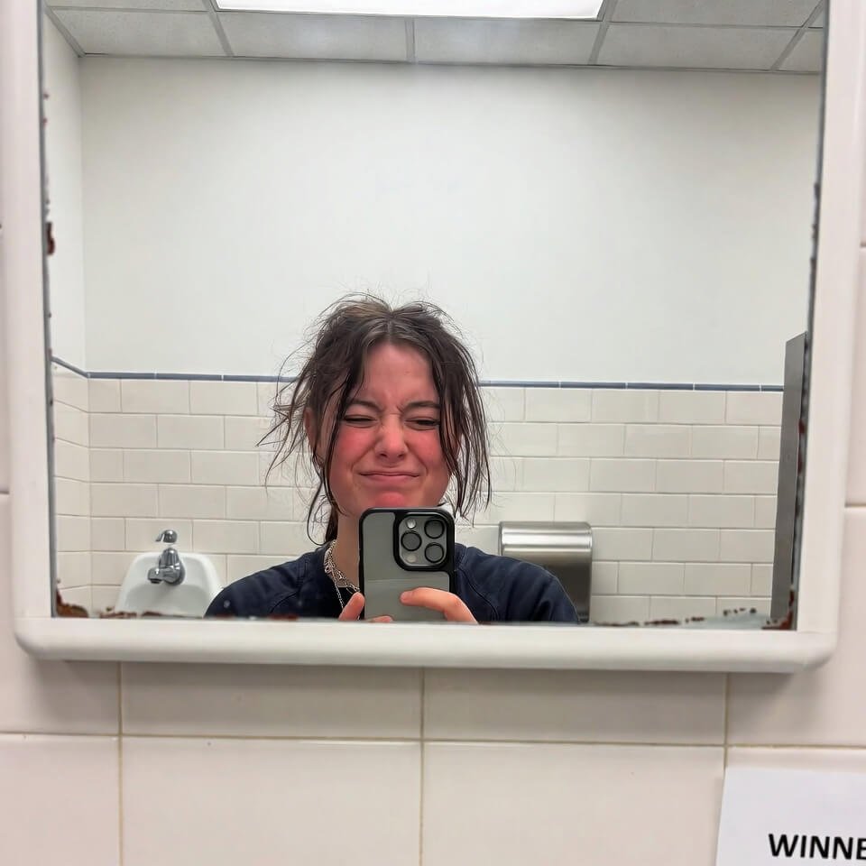 Tearful ugly-cry-laugh mirror selfie in library bathroom holding winner email